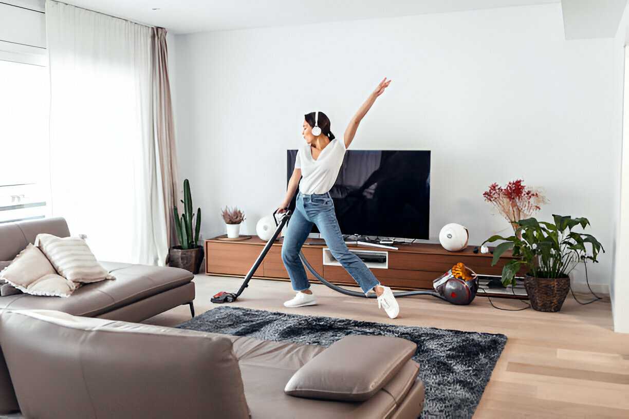 Jeune femme heureuse nettoyant le sol du salon avec un aspirateur